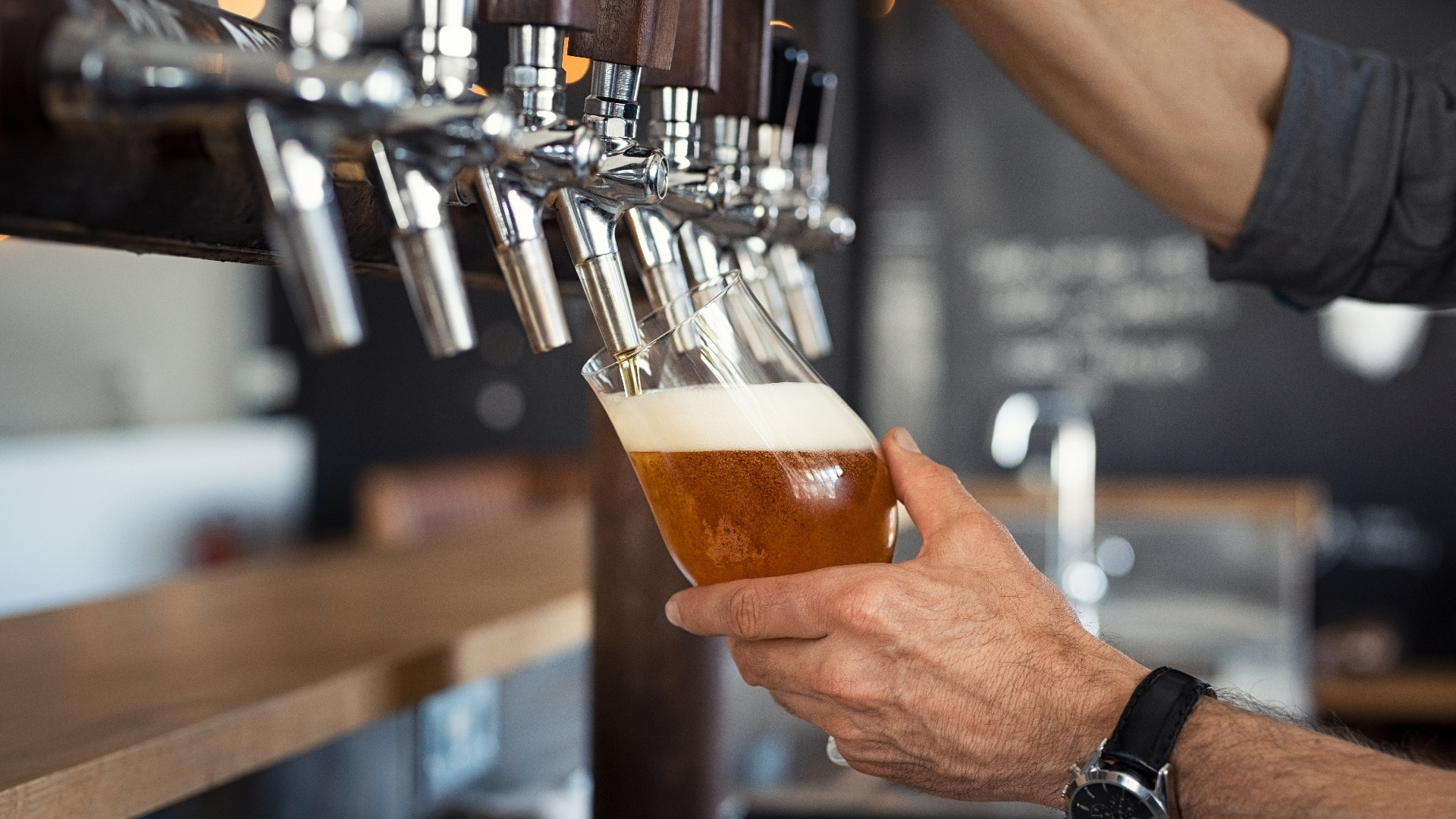 Bartender tapper en pint fra en rad med tappekraner i en pub